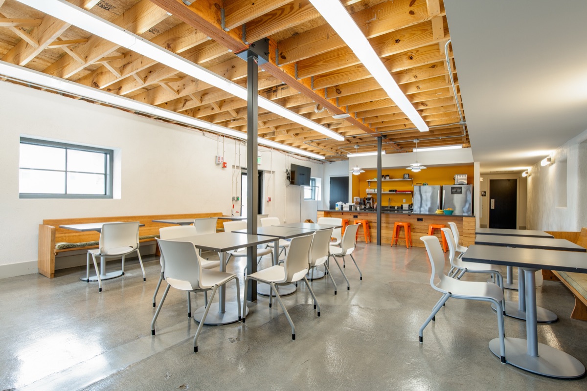 The break room: tables and chairs on polished concrete, a wood banquette along the wall, and a counter with orange stools.